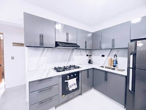Une cuisine moderne avec des meubles gris, un réfrigérateur en acier inoxydable, une cuisinière à gaz et un plan de travail en marbre.