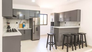 A modern kitchen with grey cabinets, a built-in island with stools, a refrigerator, and a coffee machine. - Spacious Apartment w/ Secure Private Parking (Puerto Plata)