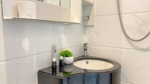 A bathroom with a black sink, a small potted plant, toiletries, and a mirror above the sink. - Warm And Homey Studio At Sky House Alam Sutera Apartment (Tangerang)