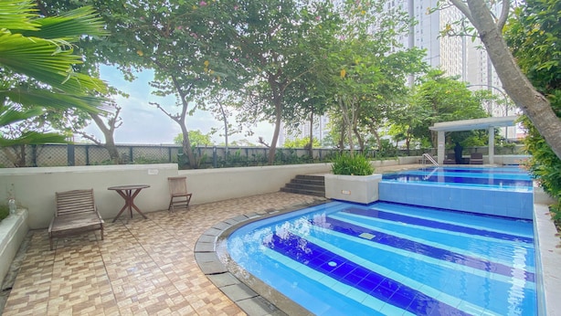 A swimming pool with a tiled deck, surrounded by greenery and a covered seating area.