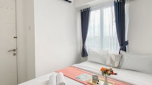 A hotel room with a bed, a window with curtains, an air conditioning unit, and a tray with a vase of flowers.