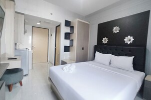 Habitación de hotel con una cama grande, un escritorio con silla, un armario y un baño visible a través de una puerta abierta.