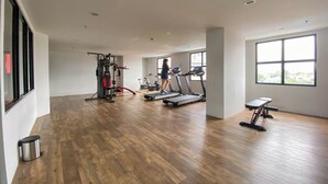 A spacious gym with wooden flooring, various exercise machines, and large windows providing natural light. - Cozy Living Studio The Alton Apartment (Semarang)