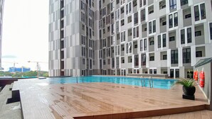 A modern building with a rooftop pool area featuring a wooden deck and a swimming pool. - Cozy Living Studio The Alton Apartment (Semarang)
