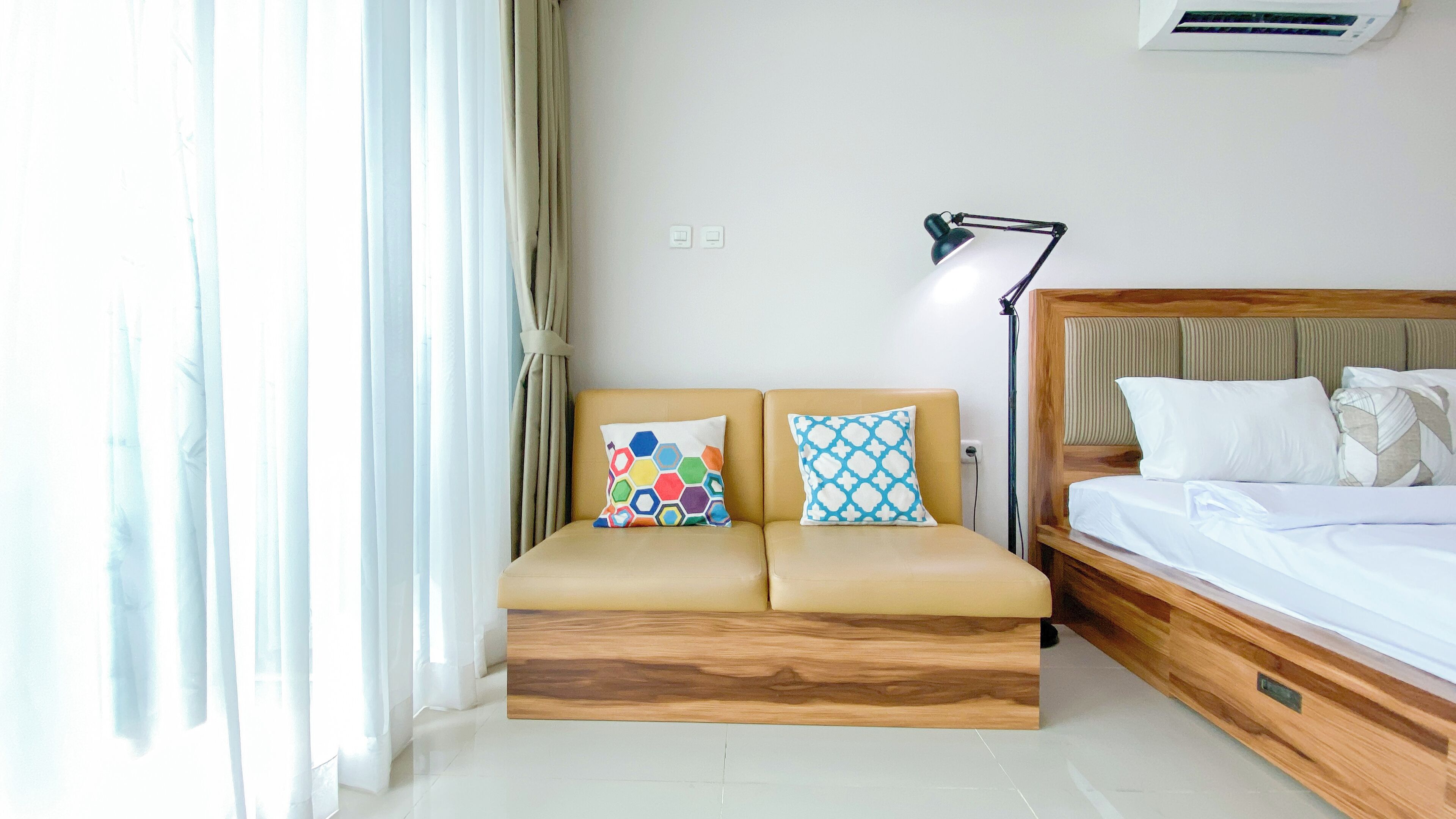 Una habitación de hotel moderna con un sofá cama, una mesita de noche, una lámpara y un equipo de aire acondicionado.