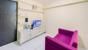 Una sala de estar con un televisor sobre un mueble blanco, un sillón rosa y una puerta.