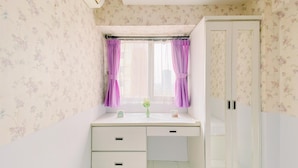 Un dormitorio con una cama individual, una mesita de noche, una ventana con cortinas moradas y un armario.