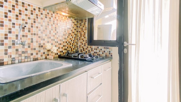 Una cocina con salpicadero de azulejos, un lavamanos de acero inoxidable, una estufa a gas y armarios de colores claros.
