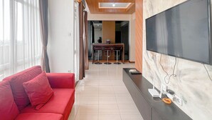 Un salon moderne avec un canapé rouge, un téléviseur à écran plat fixé sur un mur de marbre, et un coin cuisine à l’arrière-plan.