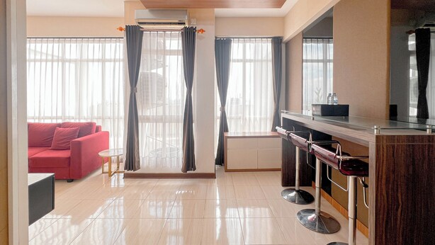 Une chambre d’hôtel moderne avec un canapé rouge, une petite table, un miroir et un coin bar équipé de tabourets.