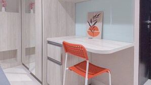 Una habitación moderna con un escritorio blanco, una silla naranja, una estantería de pared y un adorno con diseño de hoja y sol.