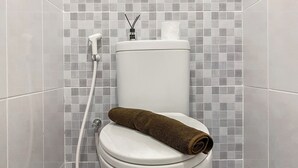 A toilet with a towel on it, a toilet paper holder, and a bidet attachment. - Serene Living Studio Tokyo Riverside Pik 2 Apartment (Teluknaga)