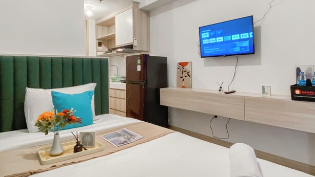 A hotel room with a bed, a TV mounted on the wall, a small kitchenette, and a bathroom visible through an open door. - Serene Living Studio Tokyo Riverside Pik 2 Apartment (Teluknaga)