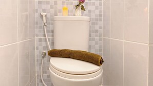 Des toilettes avec une serviette sur le siège, une bougie et une fleur dans un vase posé sur le réservoir.