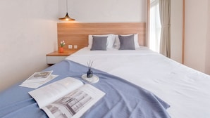 Ein ordentlich bezogenes Bett mit Holz-Kopfteil, ein Nachttisch mit Lampe und ein Fenster mit Vorhängen.