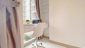 A modern hotel room with a white chair, a small potted plant, and a window with a view of a building. - Warm And Simply Look Studio Apartment Tokyo Riverside Pik 2 (Teluknaga)