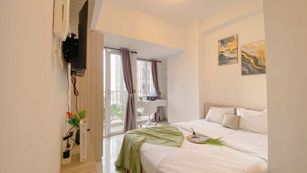 A bedroom with a bed, a desk, a chair, a TV, and a window with curtains. - Warm And Simply Look Studio Apartment Tokyo Riverside Pik 2 (Teluknaga)