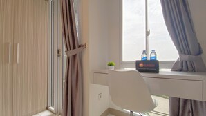 A hotel room with a desk, a chair, a window with curtains, and a box labeled 'Travelio' with water bottles on it. - Warm And Simply Look Studio Apartment Tokyo Riverside Pik 2 (Teluknaga)