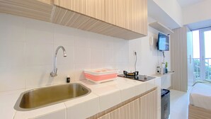 A modern kitchen with a stainless steel sink, a pink and white storage bin, and a flat-screen TV mounted on the wall. - Warm And Simply Look Studio Apartment Tokyo Riverside Pik 2 (Teluknaga)