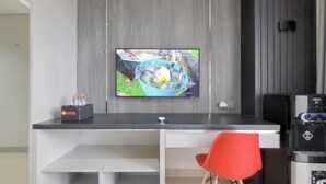 A modern kitchen with a flat-screen TV mounted on the wall, a red chair, and a coffee machine. - Homey And Scenic Studio At Patraland Amarta Apartment (Ngaglik)