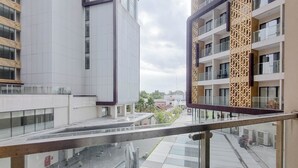 A modern building with a glass facade, a central courtyard with a fountain, and a view of surrounding buildings. - Homey And Scenic Studio At Patraland Amarta Apartment (Ngaglik)