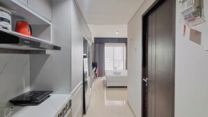 A hotel corridor with a white countertop, a black induction cooktop, and a bed with a white headboard. - Homey And Scenic Studio At Patraland Amarta Apartment (Ngaglik)