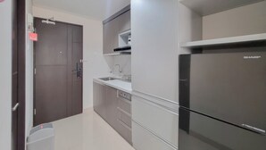 A modern kitchen with a stainless steel refrigerator, a built-in sink, and a dark wooden door. - Homey And Scenic Studio At Patraland Amarta Apartment (Ngaglik)