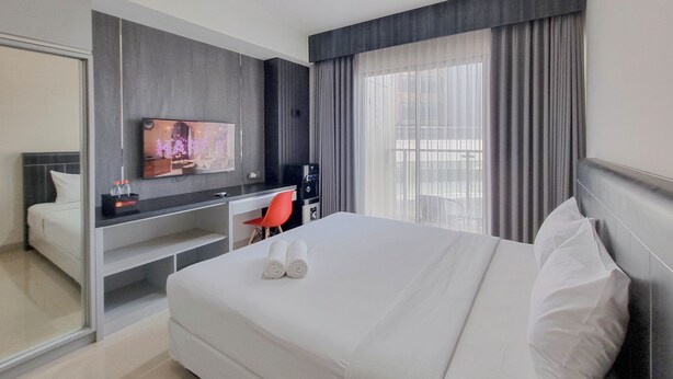 A hotel room with a bed, a desk, a television, and a window with curtains. - Homey And Scenic Studio At Patraland Amarta Apartment (Ngaglik)