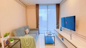 A modern living room with a sofa, a coffee table, a TV, and a view of a cityscape through large windows. - Comfort Living 2Br Apartment At Casa Grande Residence (Jakarta)
