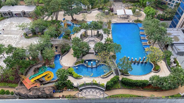 A large outdoor swimming pool area with multiple water features, including a central pool, smaller pools, and a water slide. - Comfort Living 2Br Apartment At Casa Grande Residence (Jakarta)
