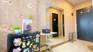Un espace d’accueil d’hôtel comprenant un mur décoratif, un comptoir d’accueil, un réfrigérateur orné d’autocollants, une plante en pot et une porte.