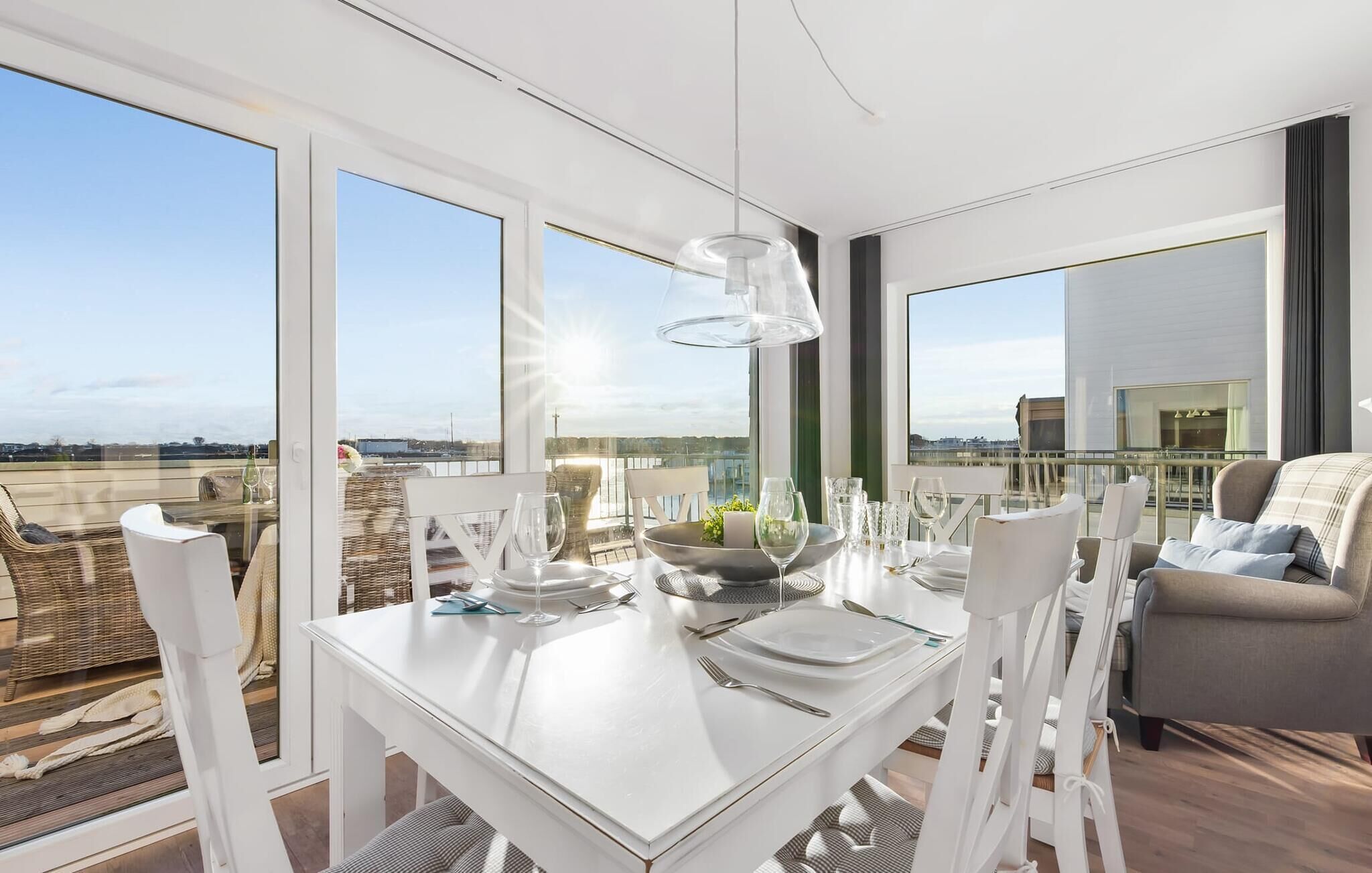 A dining area with a white table set for four, large windows offering a city view, and a modern pendant light.