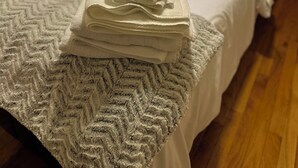 A neatly made bed with a folded white towel on the bedspread, a pillow with a word on it, and a blue pillow on the headboard.