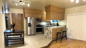 A modern kitchen with wooden cabinets, a stainless steel refrigerator, a microwave, and a granite island with bar stools.