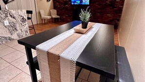 A modern dining area with a dark wooden table, a bench, and a TV mounted on a brick wall.