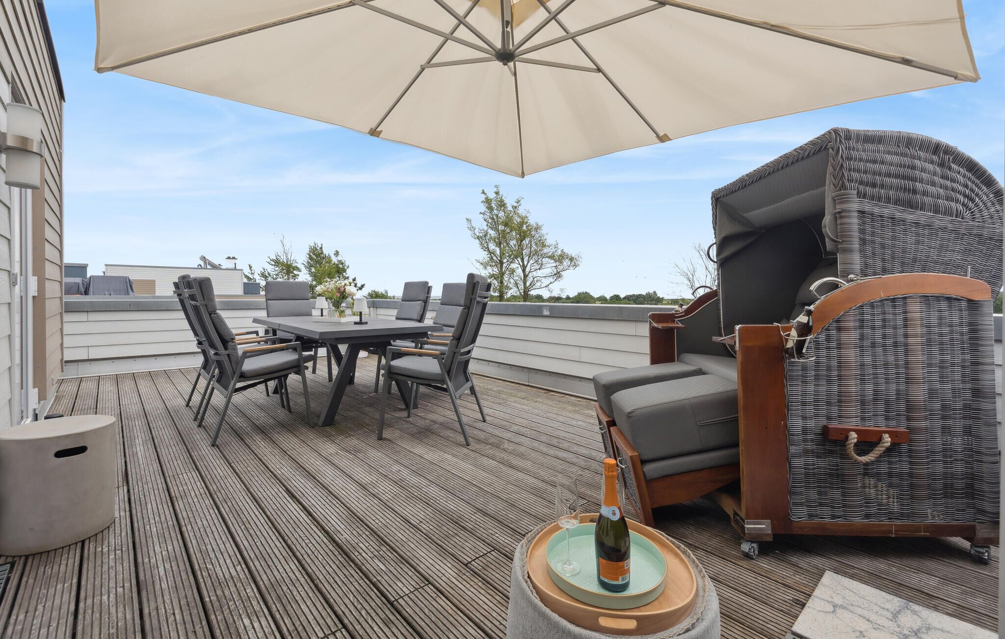 Une terrasse sur le toit avec une table et des chaises, un fauteuil en osier et une bouteille de champagne.