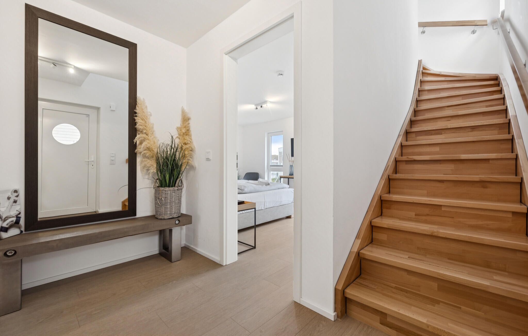 Ein modernes Interieur mit einer Holztreppe, einem großen Spiegel und einer Bank mit Pampasgras.