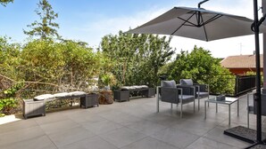 A patio with outdoor furniture, a large umbrella, and a view of trees and a building. - Cozy home in Trecastagni (Trecastagni)
