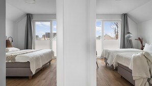 Een slaapkamer met twee bedden, een groot raam en uitzicht op gebouwen.