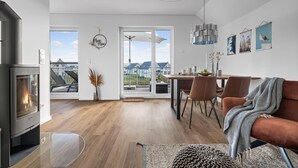 Een moderne woonkamer met een open haard, een eethoek met een tafel en stoelen, en een groot raam met uitzicht op de omgeving.