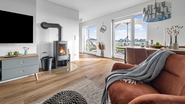 Een moderne woonkamer met een houtkachel, een flatscreen televisie en een gezellige zithoek met een bruine bank en een geborduurd plaid.