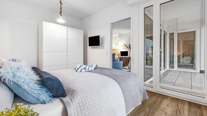 Un dormitorio moderno con cama, televisión y puerta corrediza de vidrio a un balcón.