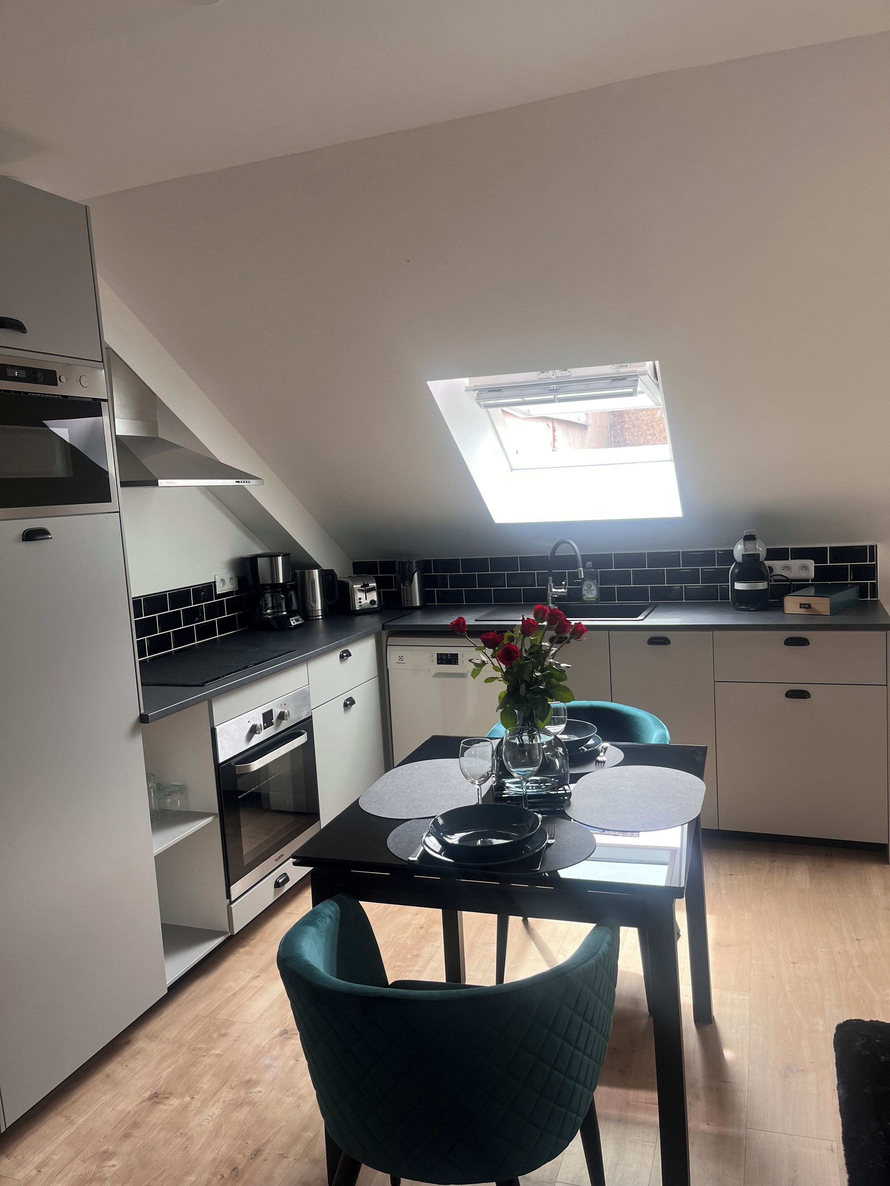 Une cuisine moderne dotée d’une verrière, un coin repas avec une table mise pour deux personnes et un lave-vaisselle.