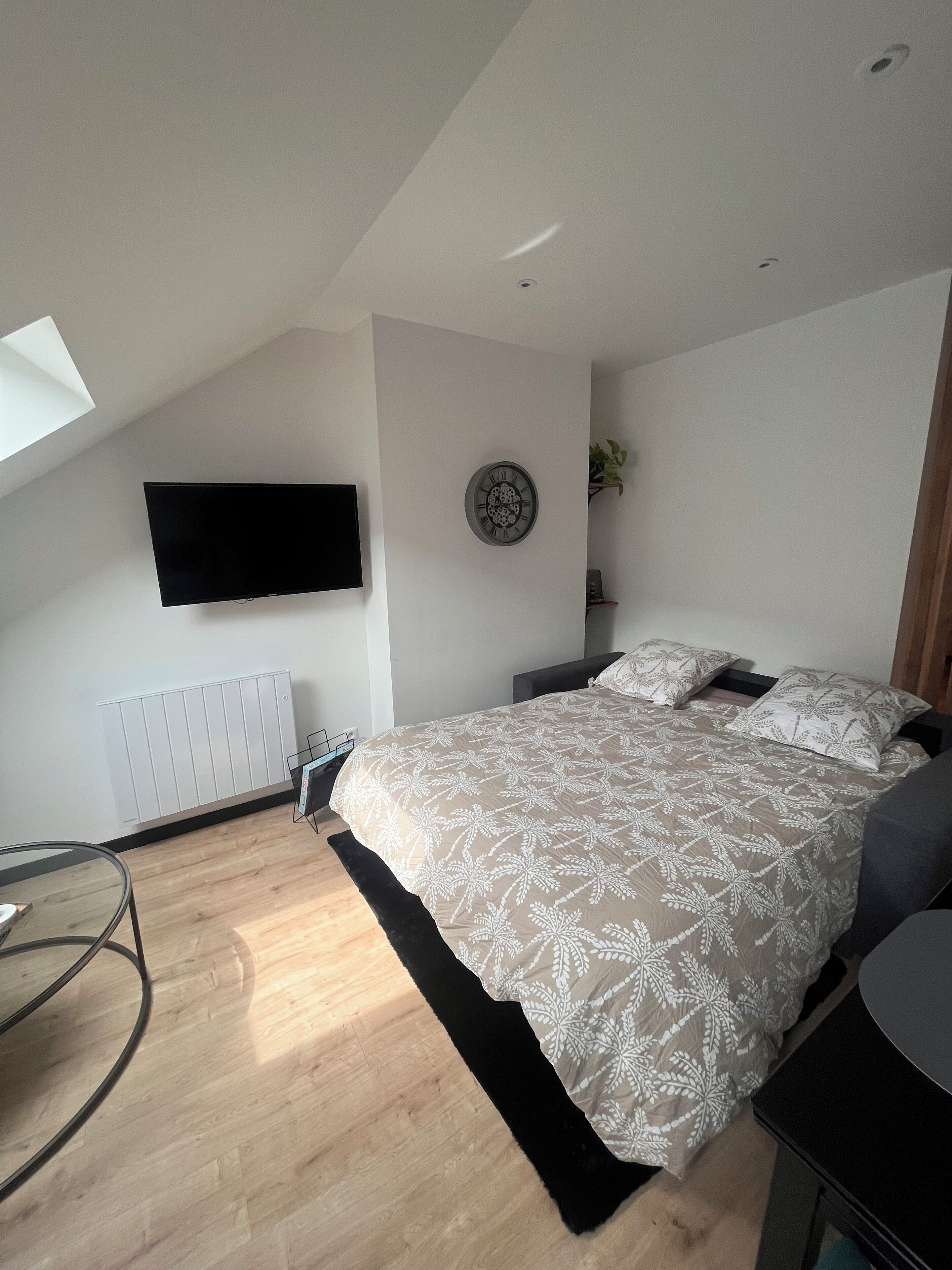 A modern bedroom with a bed, a mounted TV, a radiator, and a skylight.