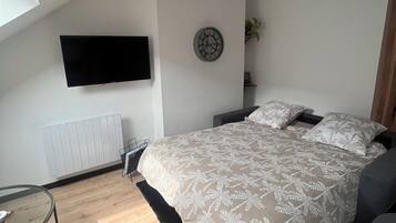 A modern bedroom with a bed, a mounted TV, a radiator, and a skylight.