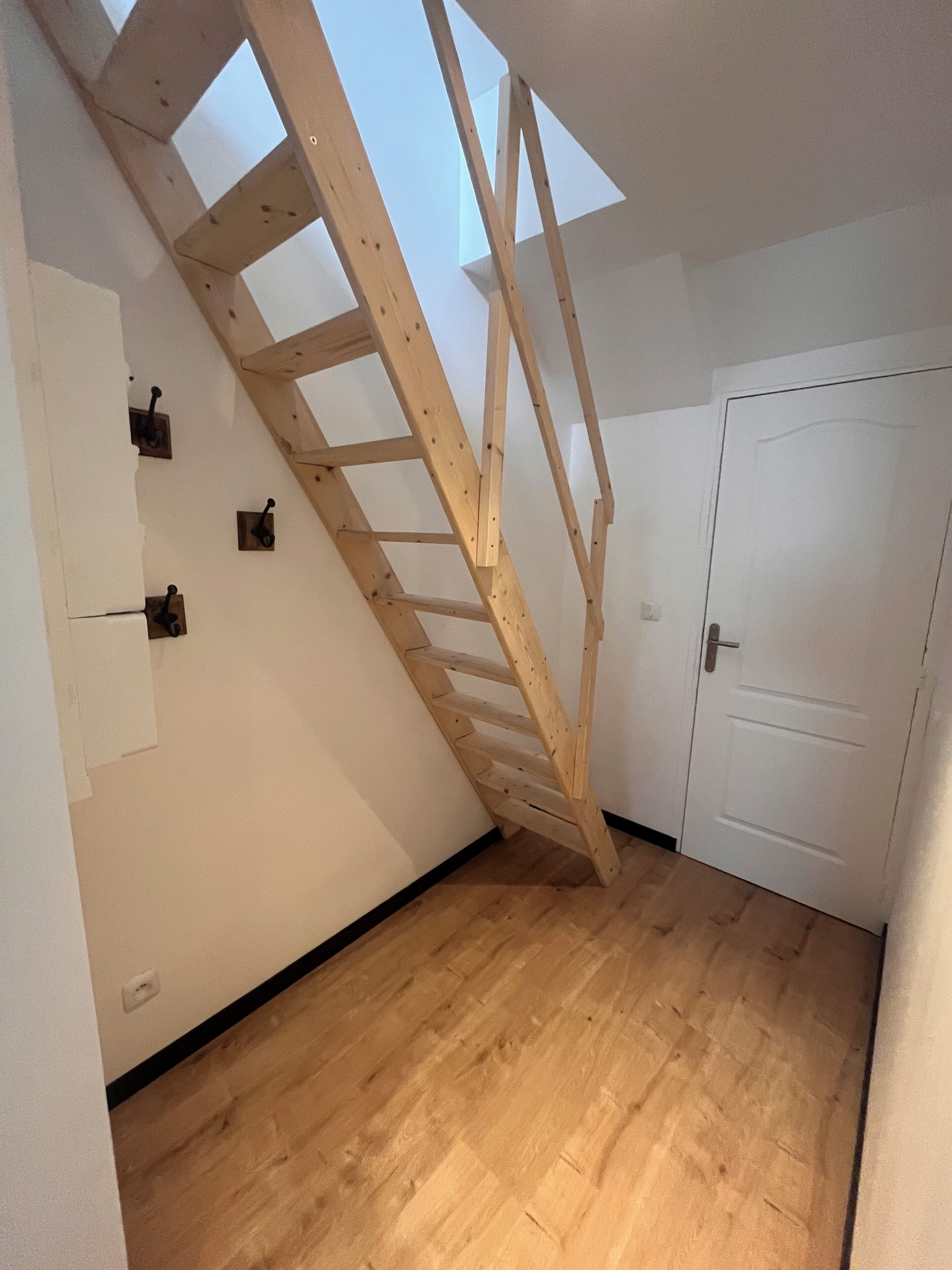 A room with a wooden staircase leading to a loft area, a white door, and a wooden floor.