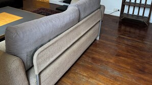 Un soggiorno con un divano grigio, una televisione su un mobile, un pavimento in legno e una porta sullo sfondo.