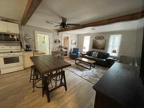 Un salón amplio con una mesa de comedor de madera, un sofá y una mesa baja. Se ve una cocina con estufa y alacenas.