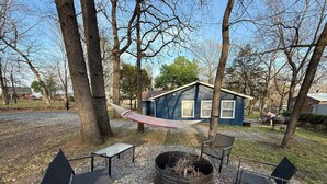 Een camping met een vuurkuil, metalen stoelen en een hangmat.