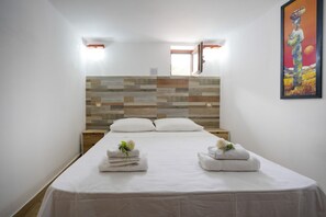 A hotel room with a bed, two pillows, a wooden headboard, a painting on the wall, and a window.